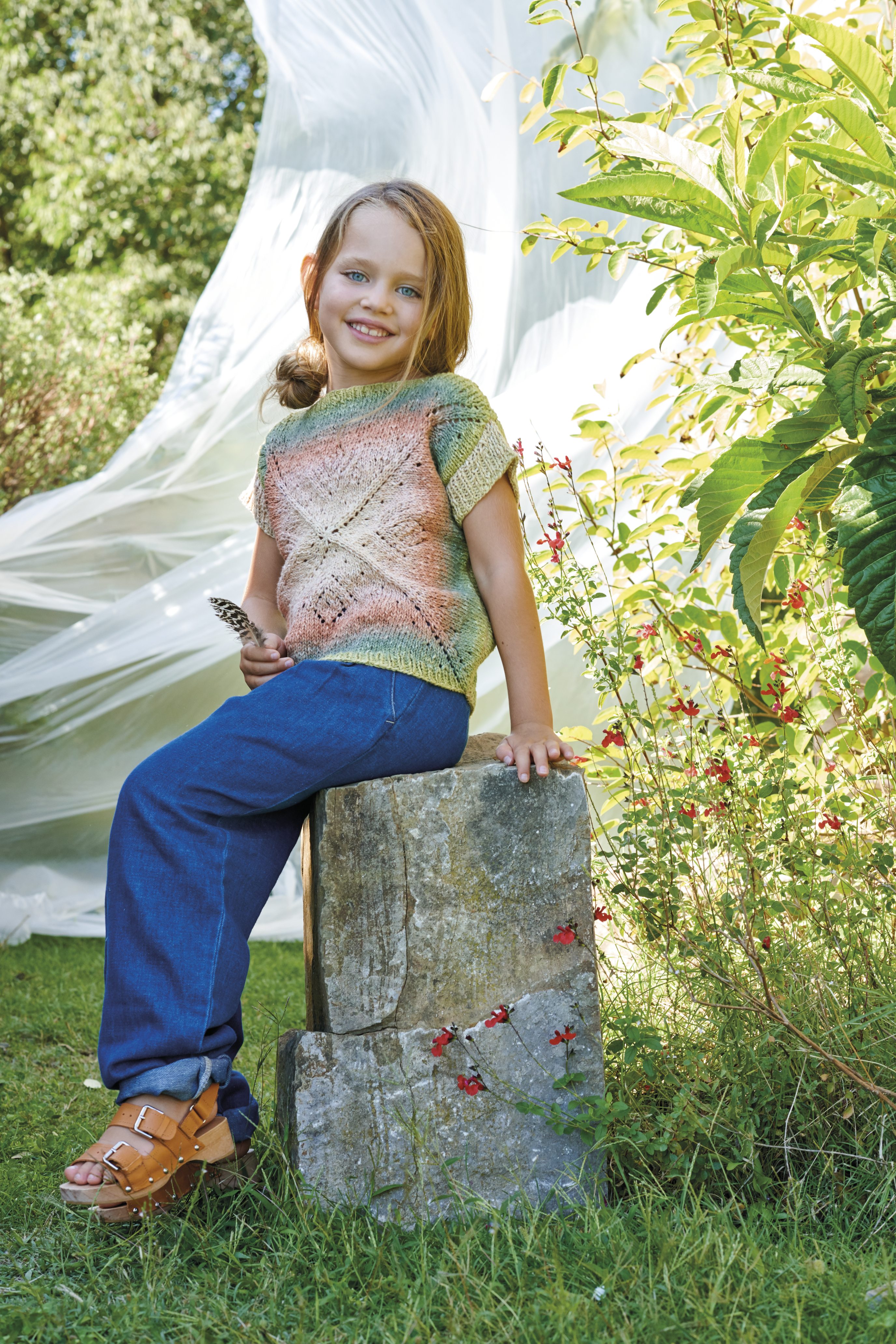 Modisches, handgemachtes Strickshirt in Pastellfarben, kombiniert mit blauer Jeans und Sandalen.