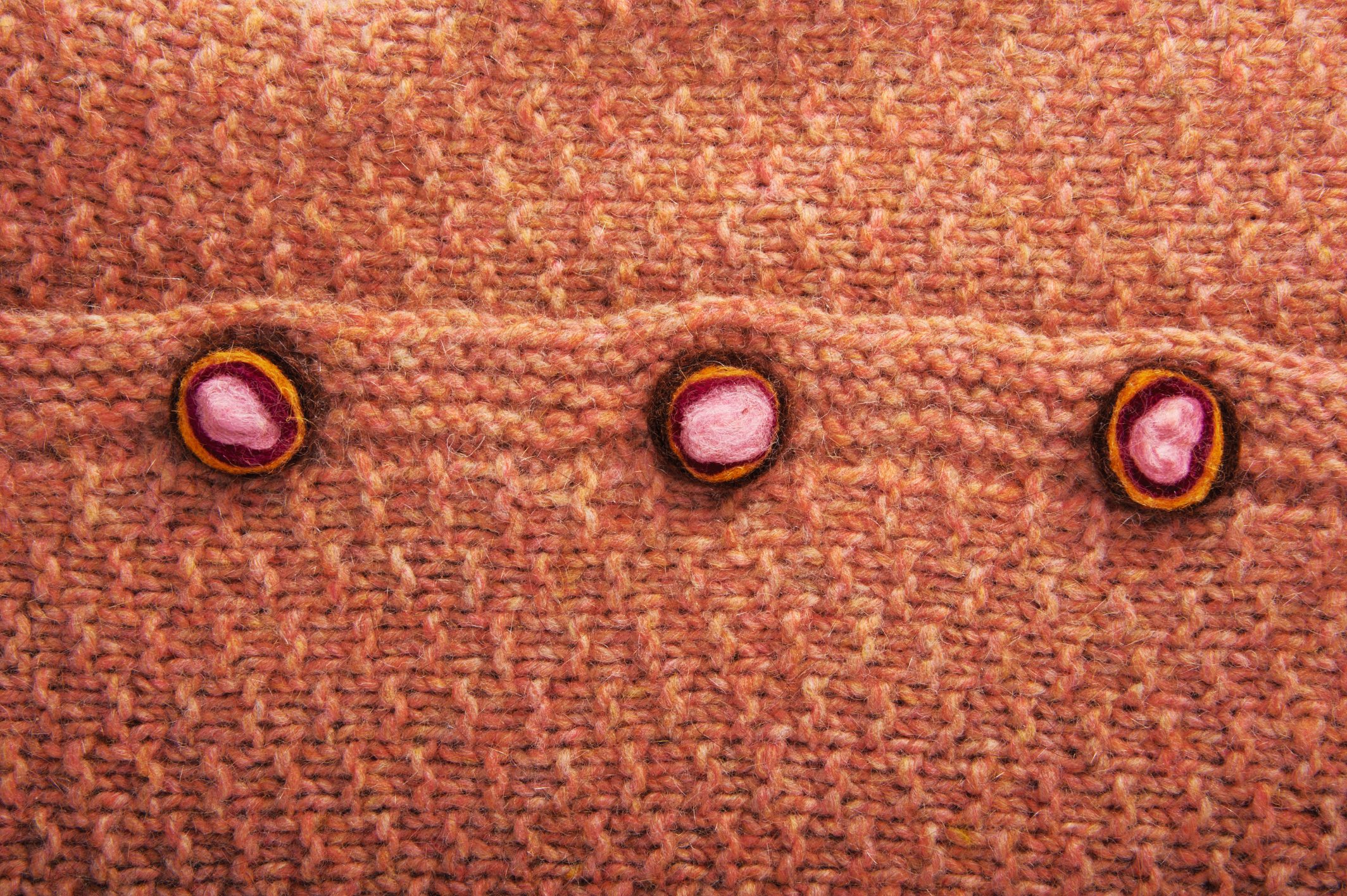 Strickstoff in warmem Orange mit dreifarbigen, handgemachten Knöpfen. Modisch, kreativ, DIY-Style.