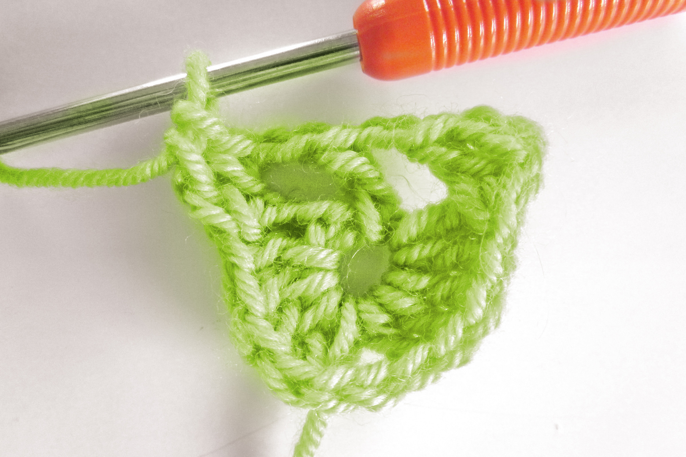 Grünes, dreieckiges Häkelstück, DIY, mit buntem Häkelnadelgriff. Handarbeit, modisch.