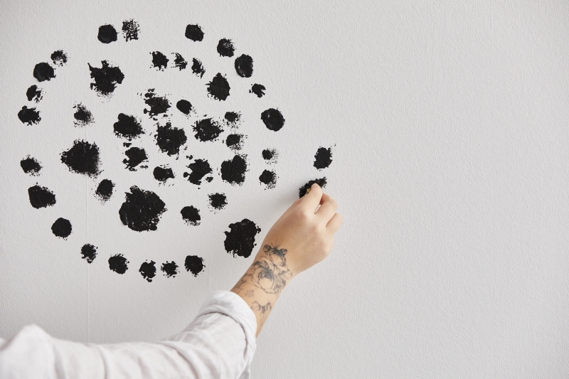 Schwarze Punkte, chaotisch verteilt. Modischer Look mit Tätowierung am Handgelenk. Handarbeit trifft Kunst.